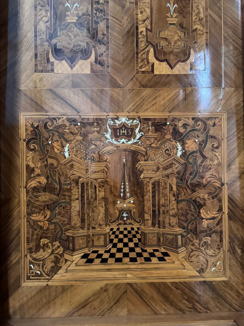An inlaid wooden panel shows a hall with a checkered floor in Trier.
