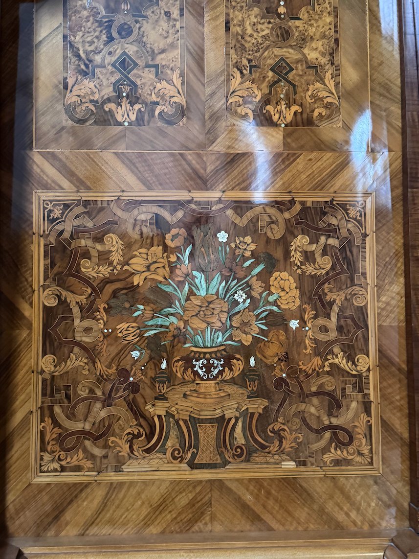 An inlaid wooden panel shows a vase of flowers on an old cabinet in Trier.