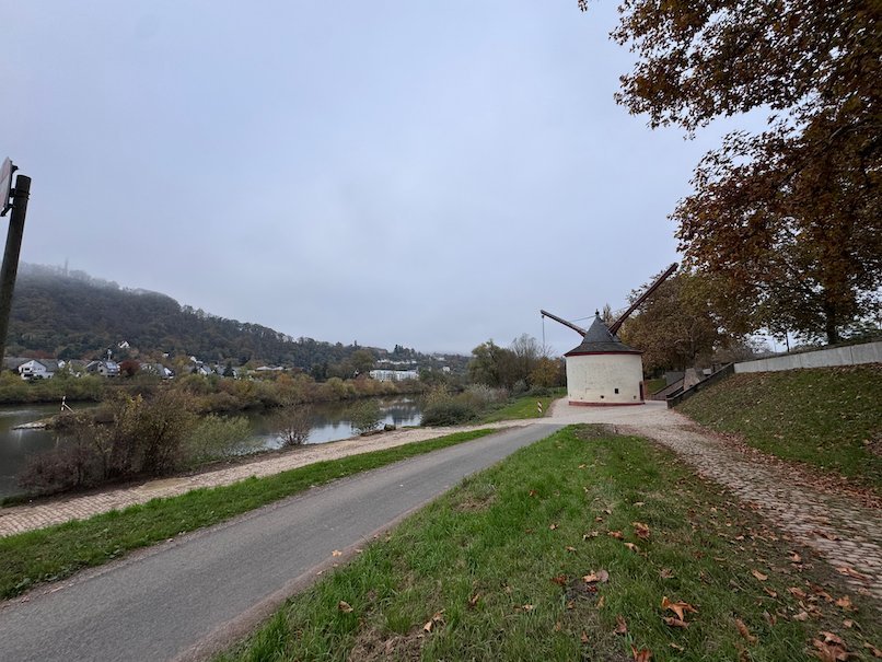 A footpath follows the Moselle past an old crane with autumn hills behind in Trier.