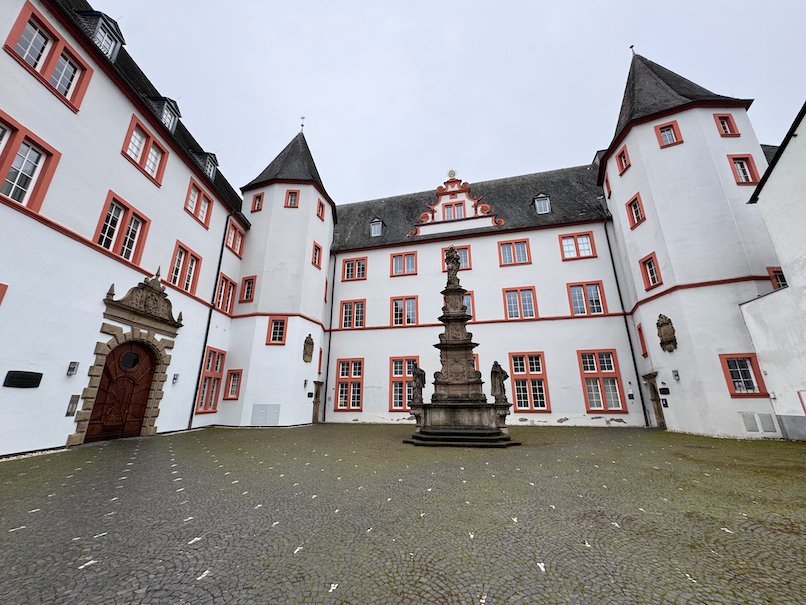 A white and red historic building with towers frames a courtyard in Trier.