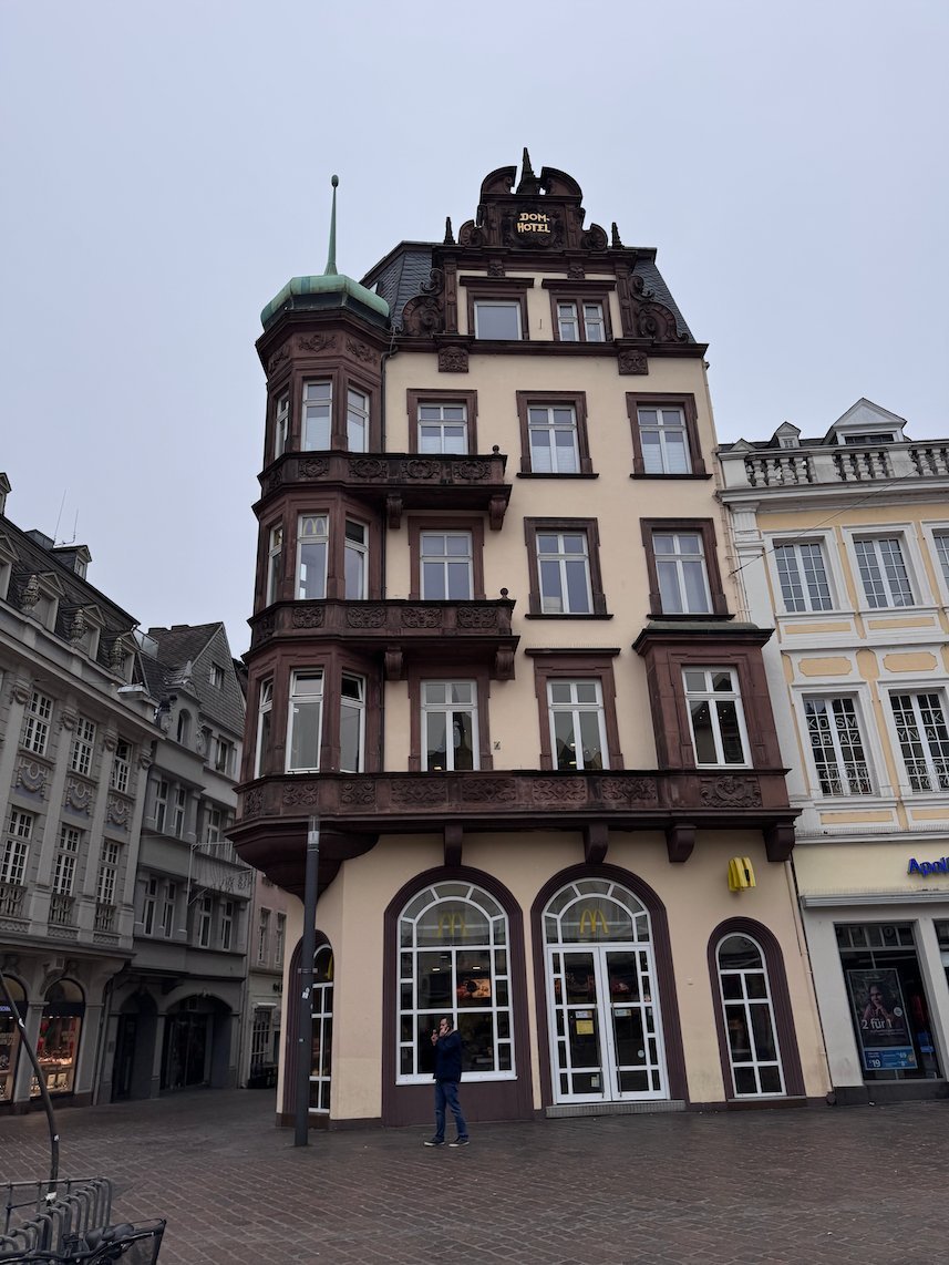 A tall ornate building with a corner bay window stands on a square in Trier.