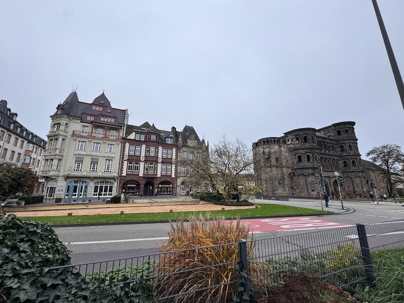 The Porta Nigra and old houses stand across a road and garden in Trier.