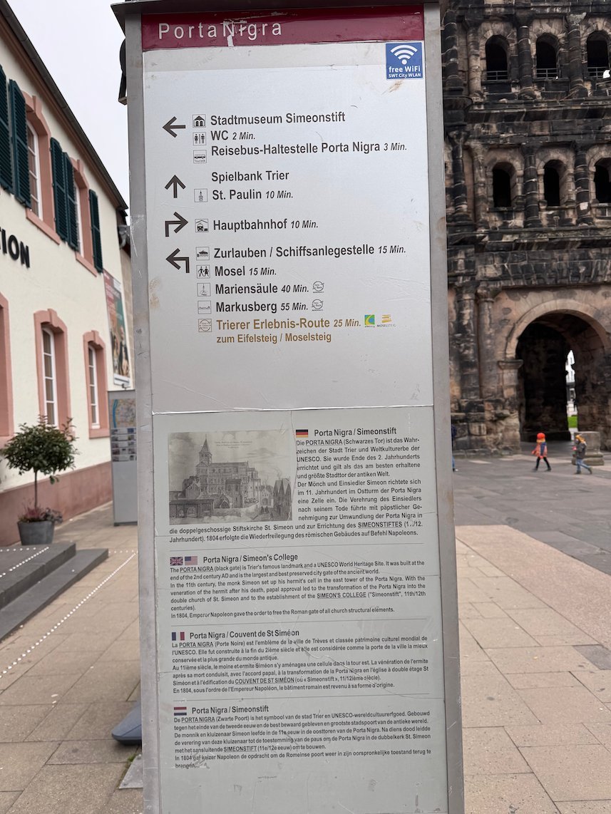 A signpost with a history text and directions stands at the Porta Nigra in Trier.