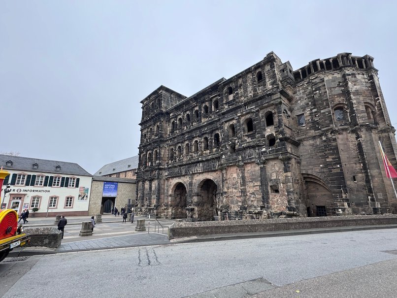 The Porta Nigra rises next to a wide street in Trier, Germany.