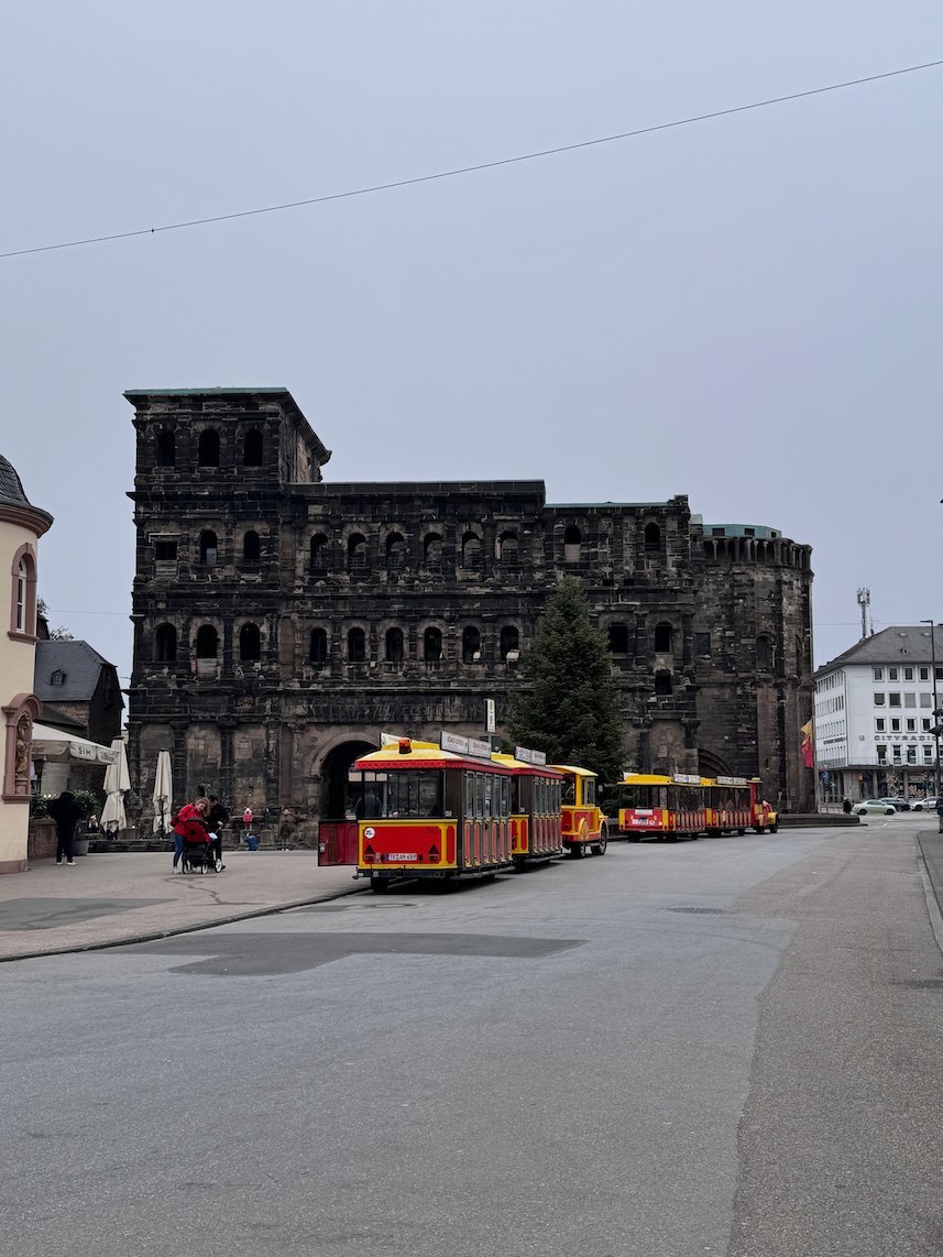 A small tourist train stands on the street in front of the Porta Nigra in Trier.