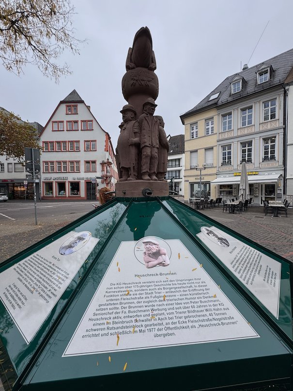 A stone sculpture stands above an information display on a square in Trier.