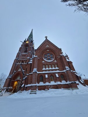 Umeå City Church, a red brick church with a tall spire and rose window, in snow
