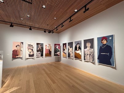 Gallery room with large portraits of women on white walls and a wooden floor