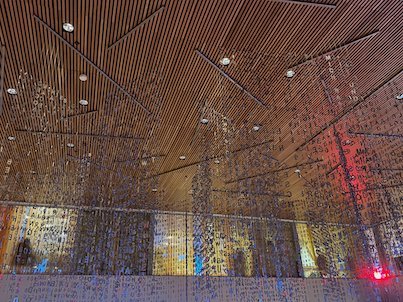 Art installation of thousands of letters hanging from a wooden ceiling, lit in red and blue