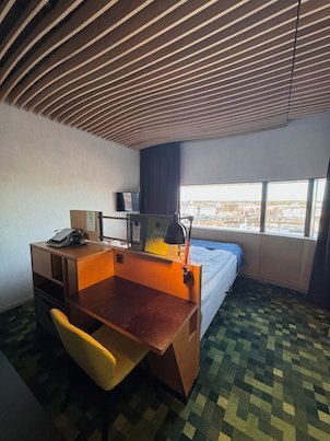 Hotel room with a wooden desk, a yellow chair and a window over Umeå