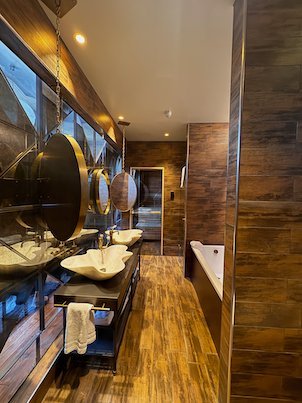 Hotel bathroom with copper sinks, round mirrors, wooden floor and a bathtub