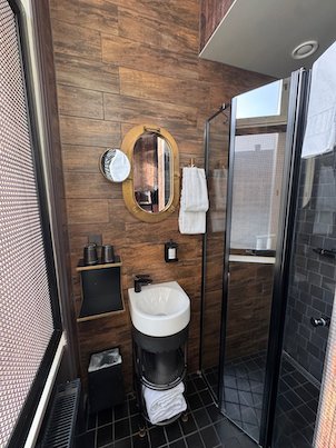 Small hotel bathroom with an oval brass mirror, a black sink and a glass shower
