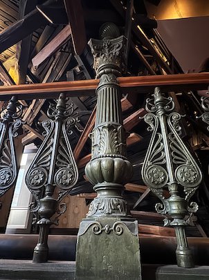 Ornate cast iron railing in front of a wooden sculpture in a hotel stairwell