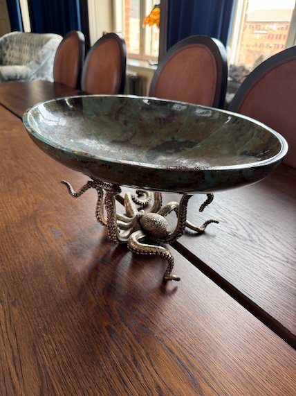 Metal bowl on octopus legs on a long wooden dining table