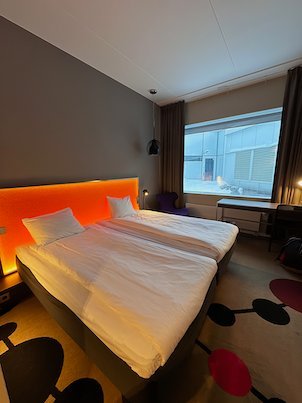 Hotel room in Umeå with a double bed, an orange lit headboard and a big window