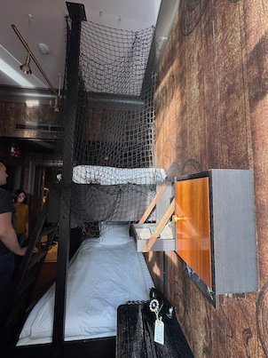 Hotel room with bunk beds behind a rope net and wooden walls, like a ship cabin