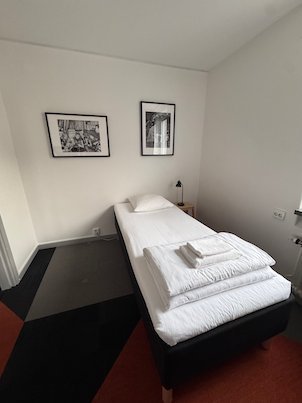 Single bed with folded towels under two black and white photos