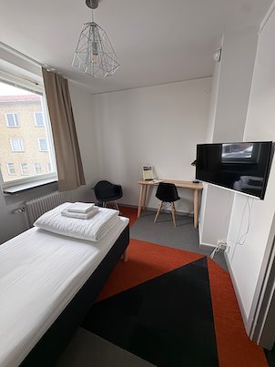 Small hotel room with a single bed, a desk, a TV and a red and black floor