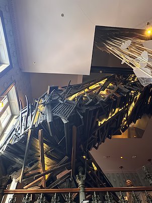 Large sculpture of broken wood pieces that hangs over a hotel stairwell