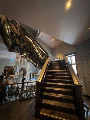 Wooden staircase under a large dark sculpture made of wood pieces in a hotel hall