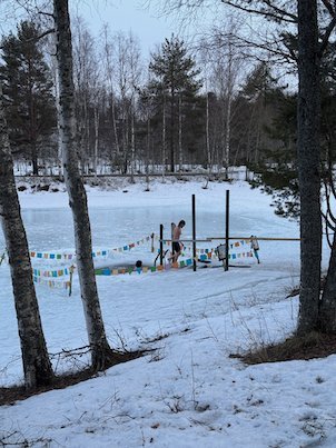 Ice bathing spot on the frozen river with a ladder, flags and a person in the water