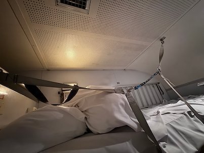 Sleeper berth on a night train with white bedding and a safety strap