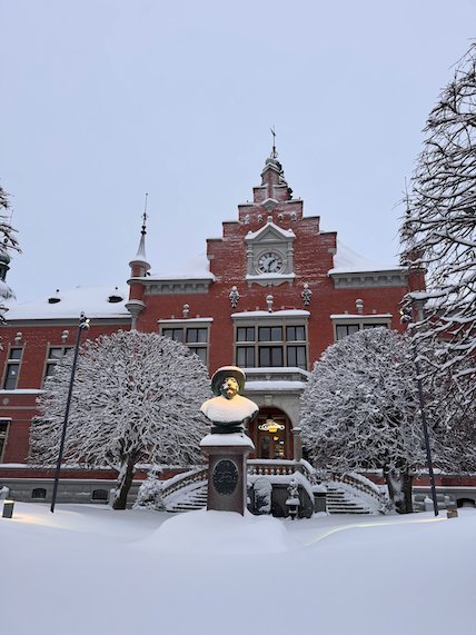 Historic red brick building with ornate gables and a bust in front, in deep snow