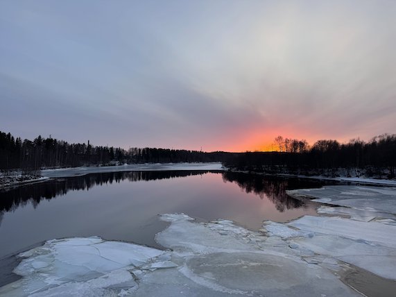 Sunset over the Ume River with floating ice and dark forest on the far bank