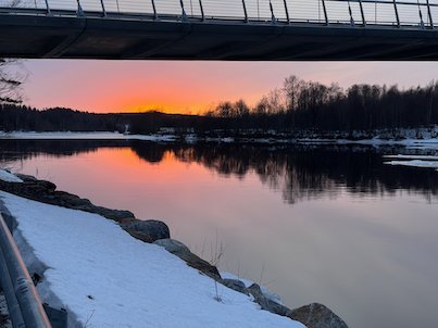 Orange sunset over the Ume River, seen from under a bridge with snow on the bank