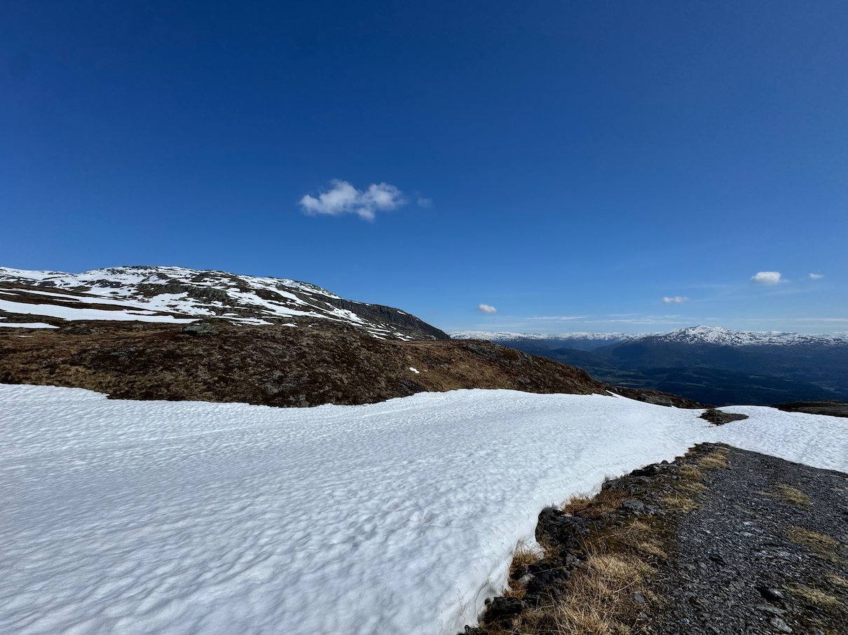 Large snowfield beside the path near Vadalseggi under a blue sky