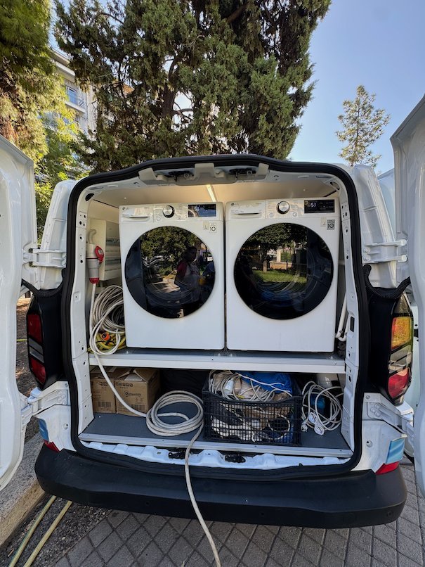 Two washing machines and cables inside the back of a mobile laundry van in Athens