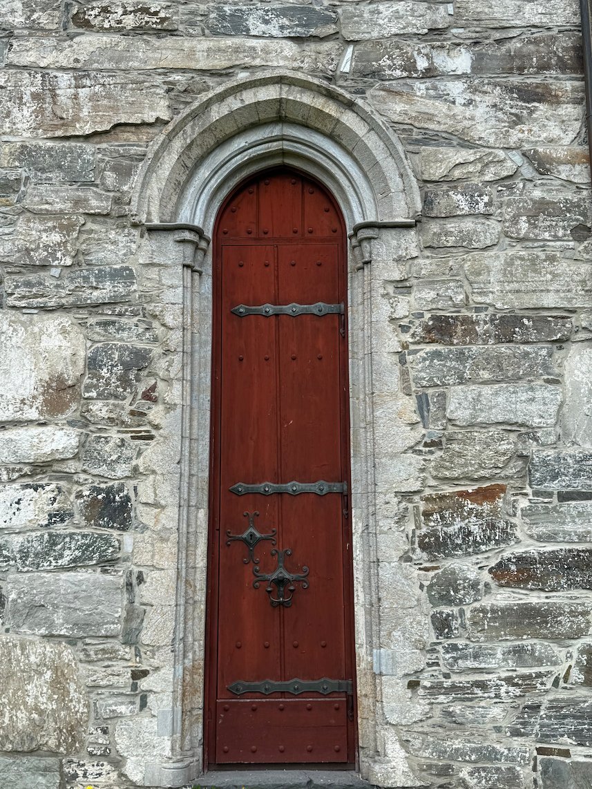 Red wooden door in a pointed stone arch at Vangskyrkja in Voss