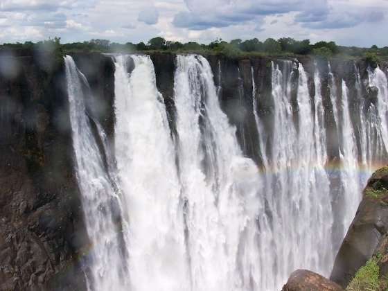 A faint rainbow forms in the spray of the white falls at Victoria Falls, Zimbabwe.
