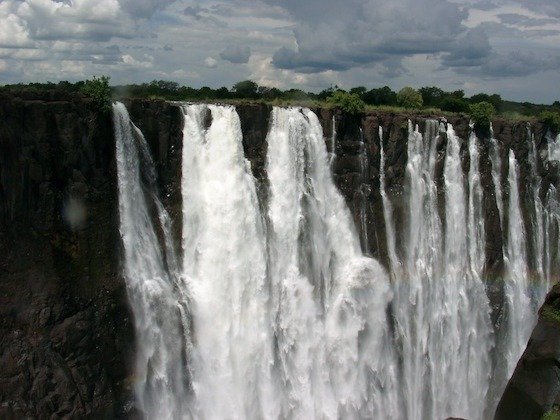 A wide wall of white water falls over dark rock at Victoria Falls, Zimbabwe.