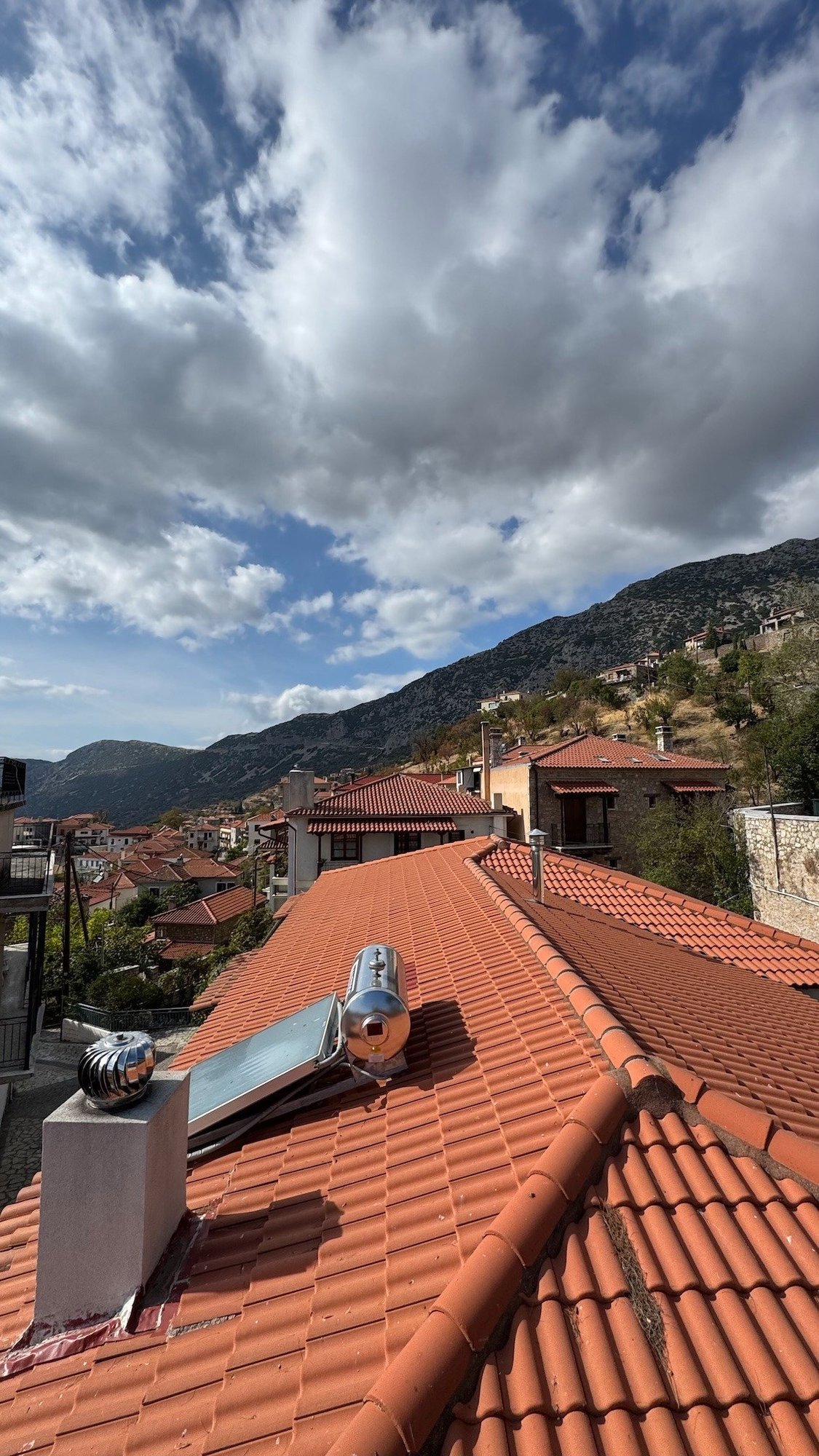 Red tile rooftops and mountains under white clouds in a village near Delphi