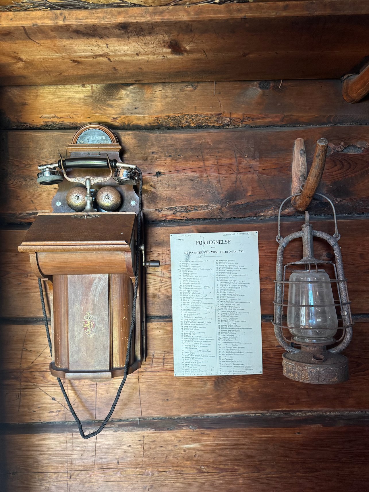 Old wall telephone, a paper notice and a lantern on a log wall at Voss Folkemuseum