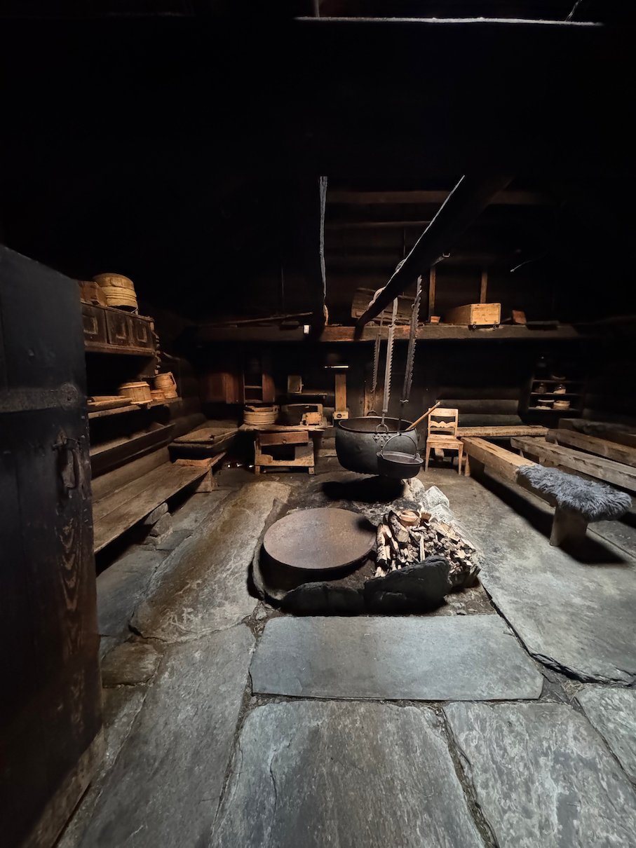 Dark interior of an old smoke house with an open hearth and wooden benches at Voss Folkemuseum