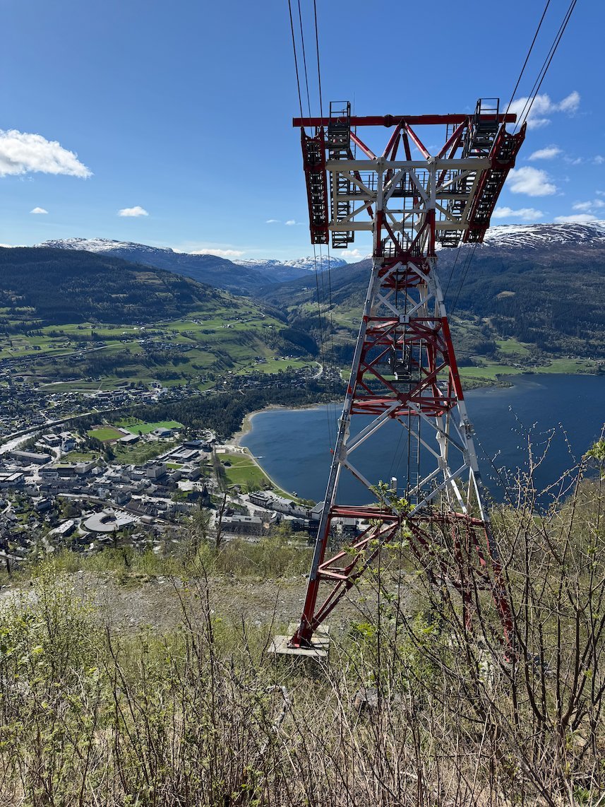 Voss Gondola mast with cables above Voss town and the lake Vangsvatnet, with snowy mountains behind