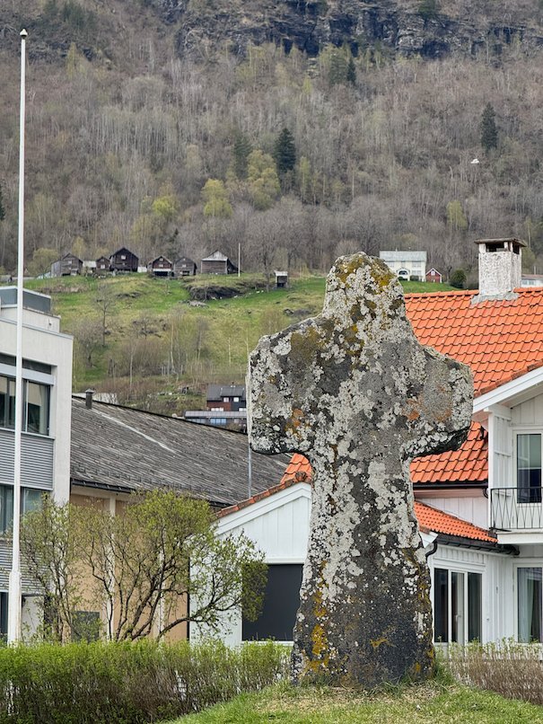 Old stone cross in Voss, with houses and green hills behind