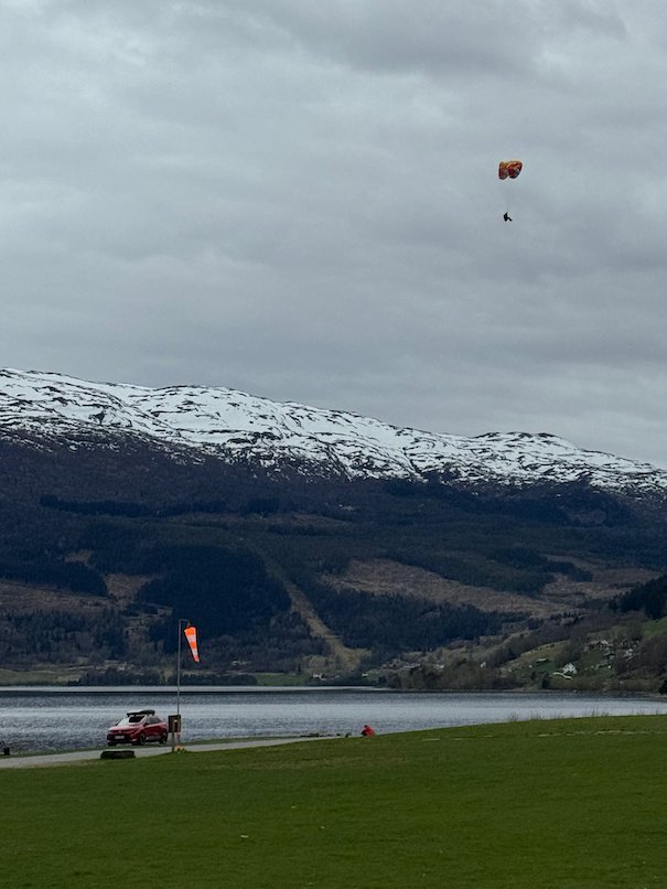 Paraglider in the sky above lake Vangsvatnet and snowy mountains in Voss