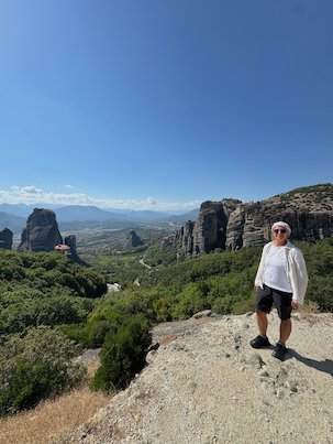 Zayera Khan in a white shirt stands on a viewpoint with the Meteora rocks behind