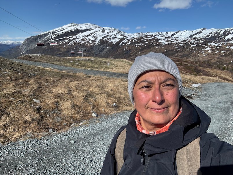 Selfie of Zayera Khan on the gravel road at Hanguren, with snowy mountains behind