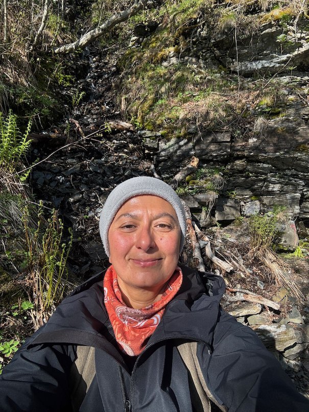 Selfie of Zayera Khan in a grey hat and an orange scarf on the forest trail to Hanguren
