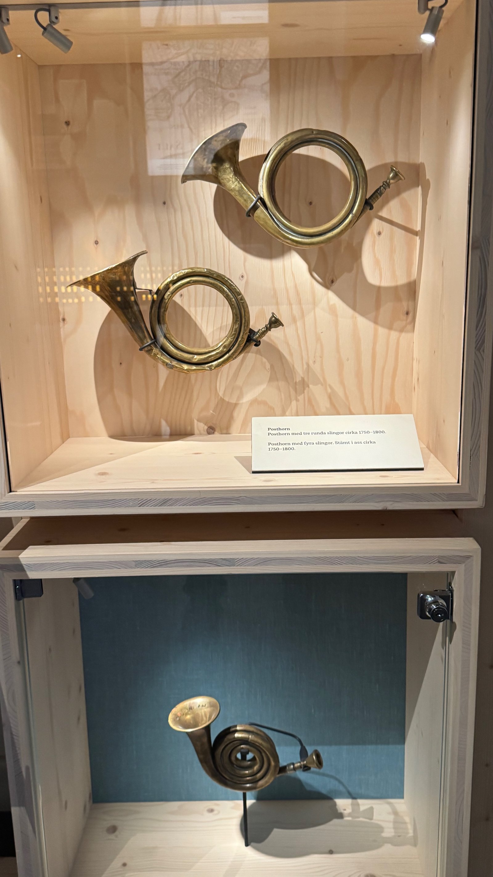 Three antique brass posthorns from around 1750 to 1800, mounted in a glass display case.