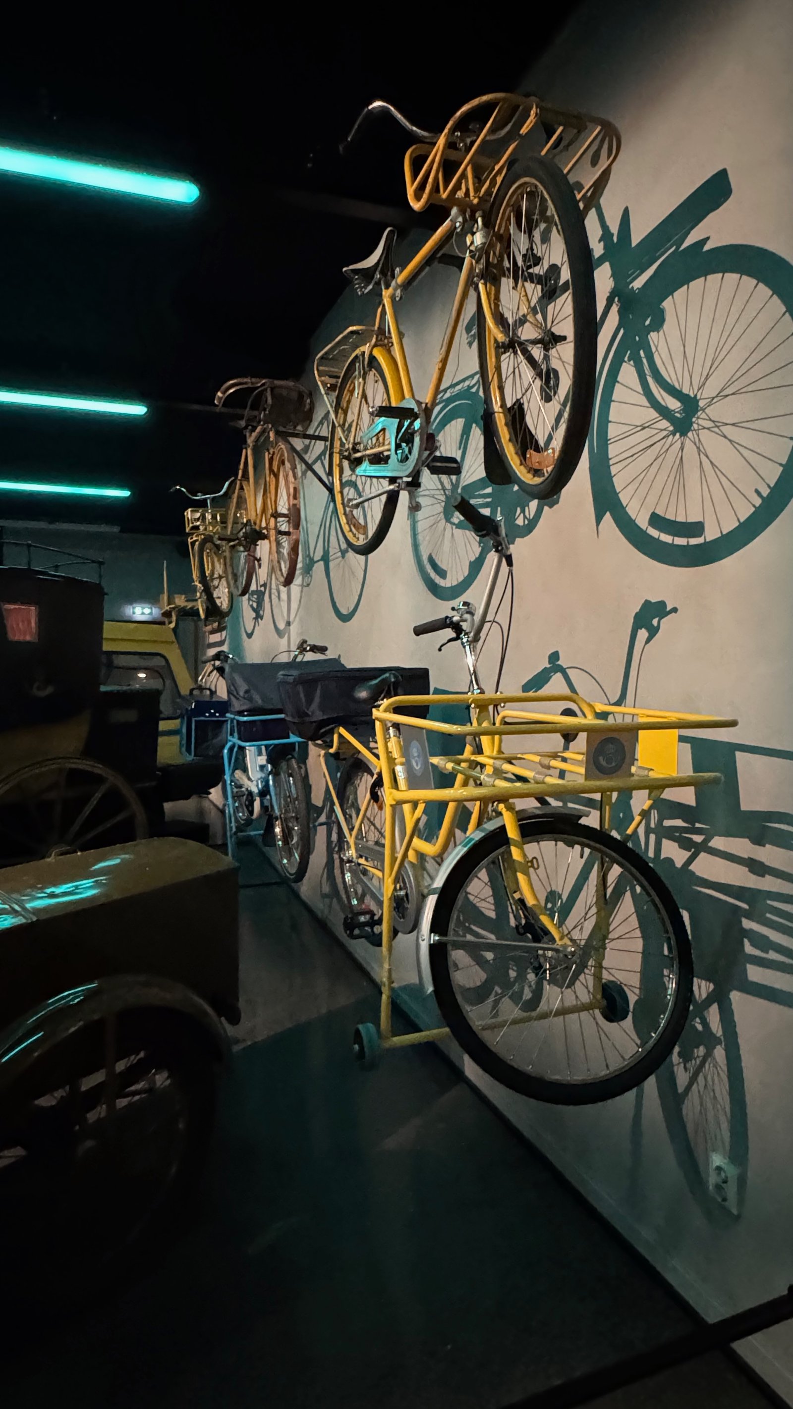 A row of vintage yellow postal delivery bicycles mounted on the wall, their shadows painted directly onto the wall behind them.