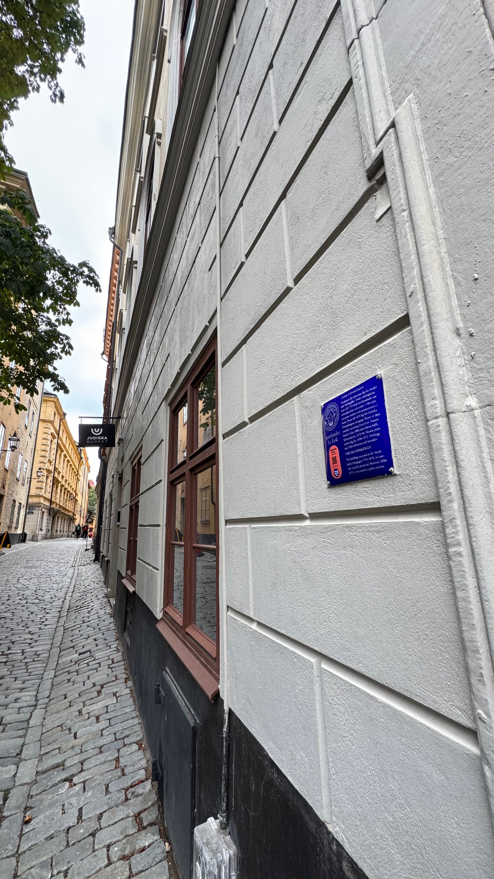 Narrow cobblestone alley in Gamla Stan, Stockholm, with pale stone buildings on either side and the Judiska Museet sign visible ahead.