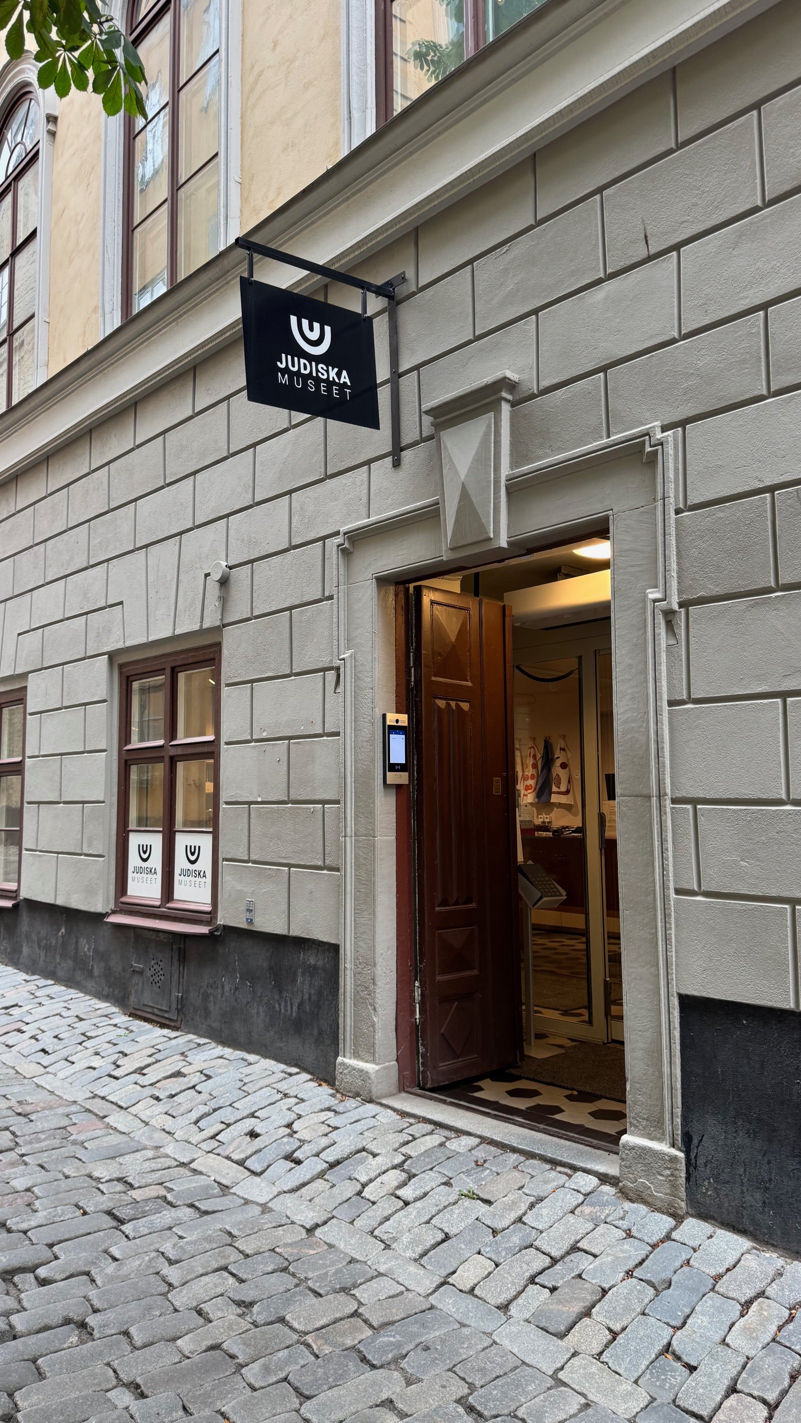 Entrance to Judiska Museet in Gamla Stan, Stockholm, with a black sign reading Judiska Museet above an open wooden door in a pale stone facade.