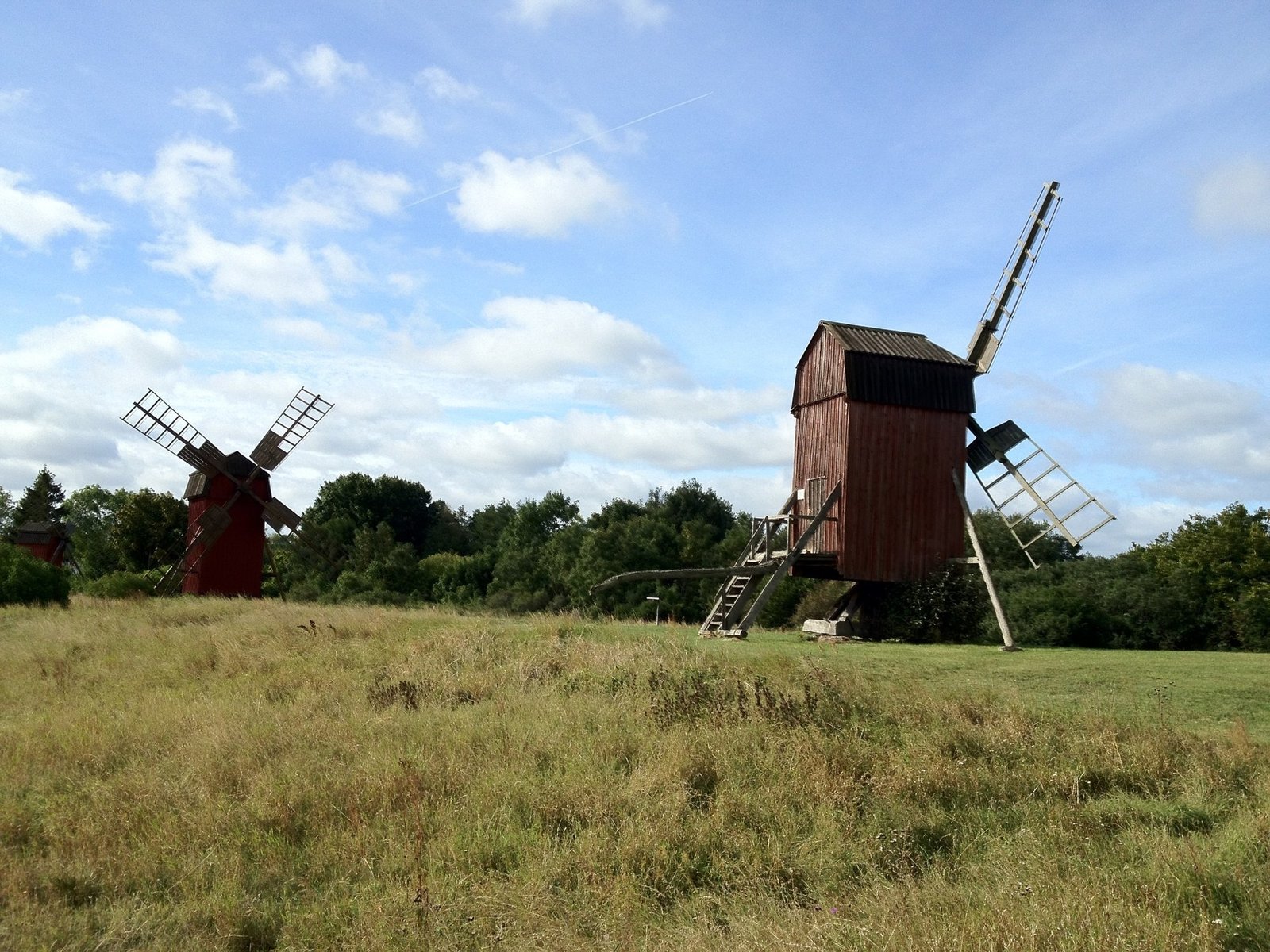 Two old wooden post windmills in a grassy field on Öland, under a blue sky with clouds.