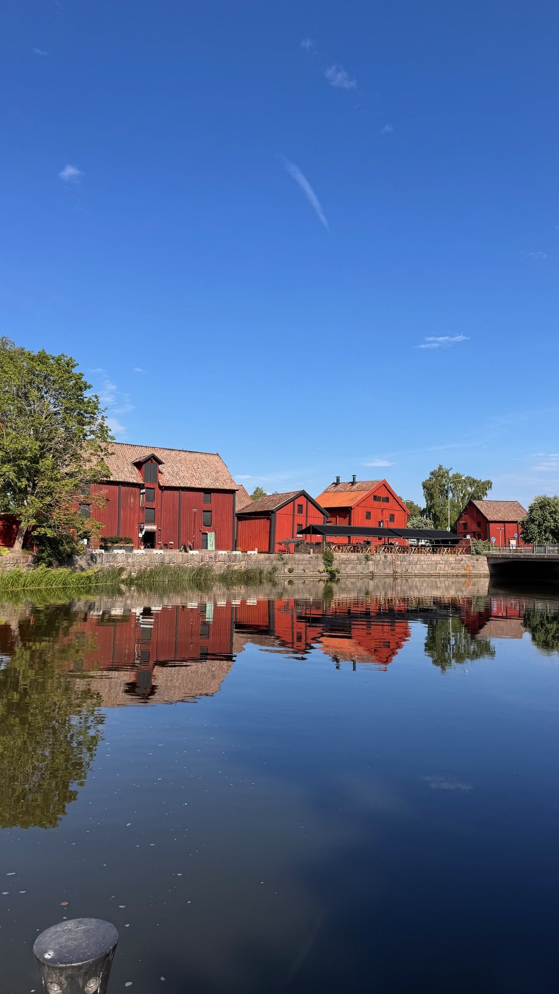 Red wooden houses reflected in calm water under a clear blue sky in Nyköping.