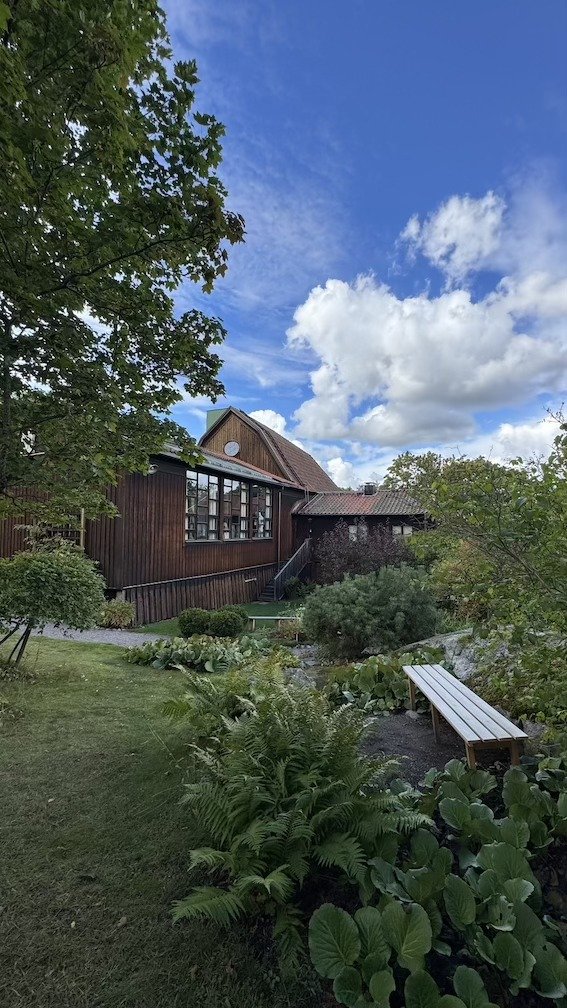 Exterior of the tarred wooden studio building at Carl Eldhs Ateljémuseum, seen from the garden under a blue sky.